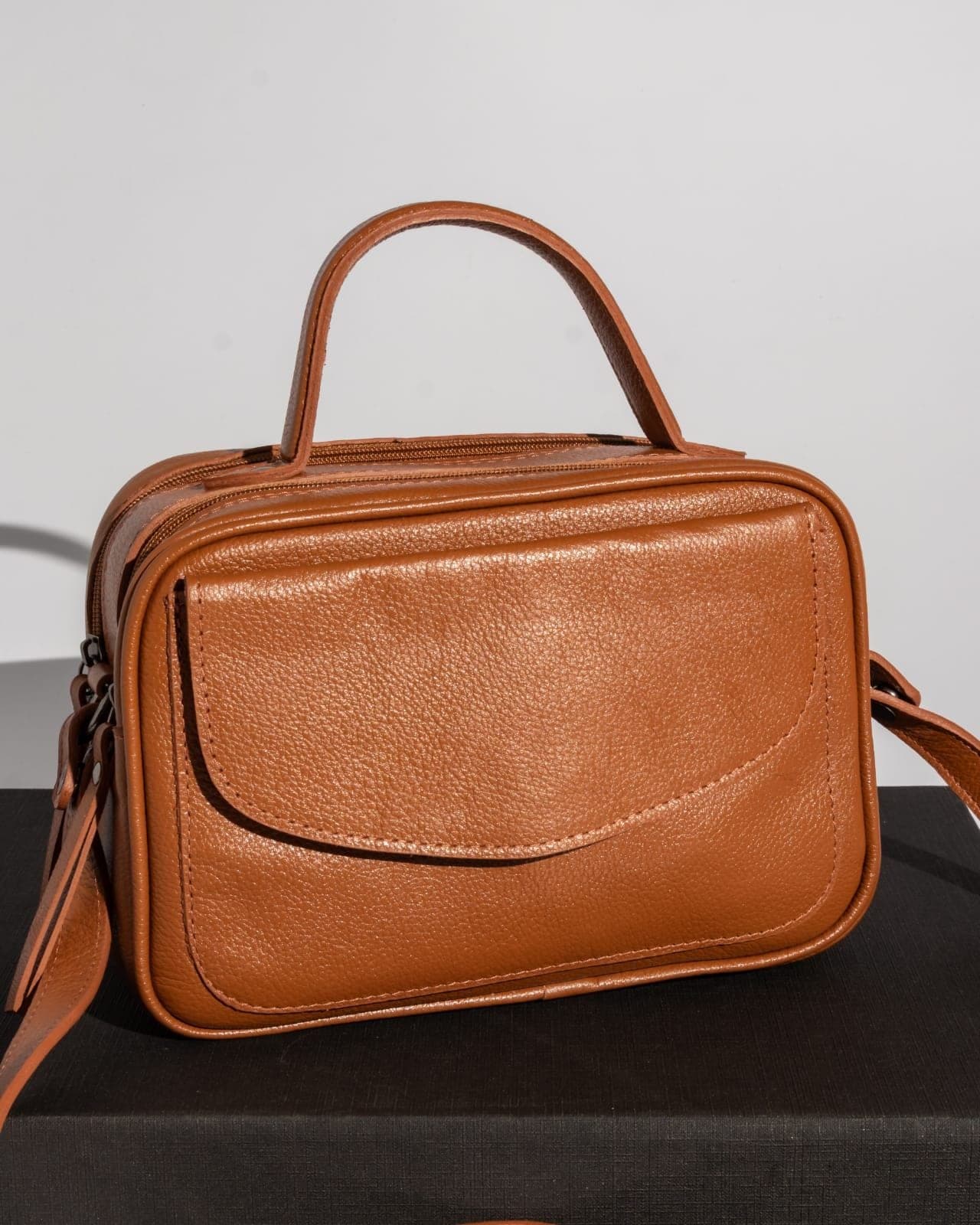 Bolsa baú em tom caramelo, com alça de mão e bolso frontal com aba